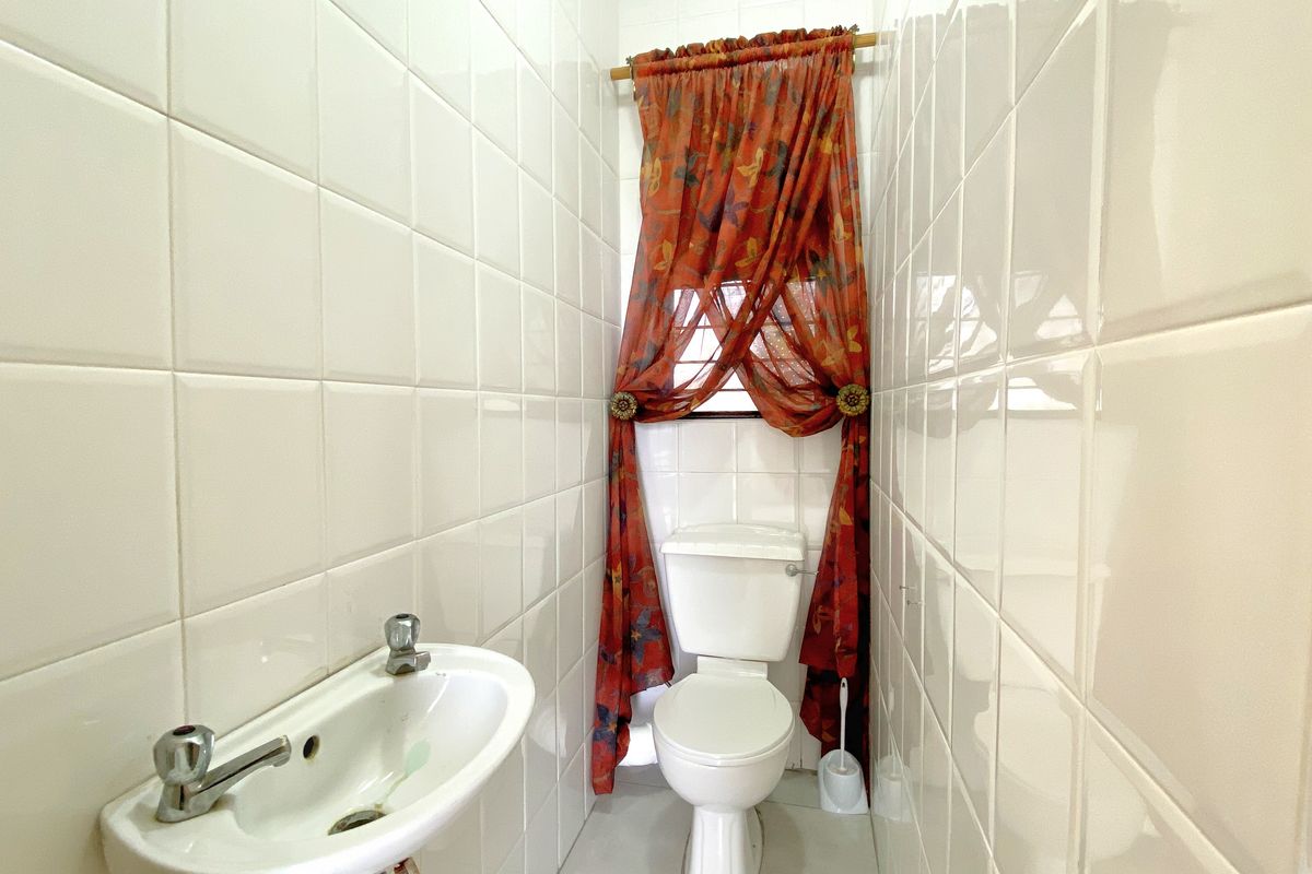A compact guest bathroom featuring white wall tiles, a standard toilet, and a small wall-mounted basin.