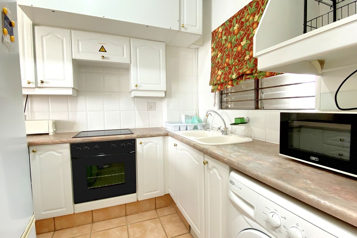 A functional kitchen featuring white cabinetry, a built-in oven with hob, double sink, and space for under-counter appliances.