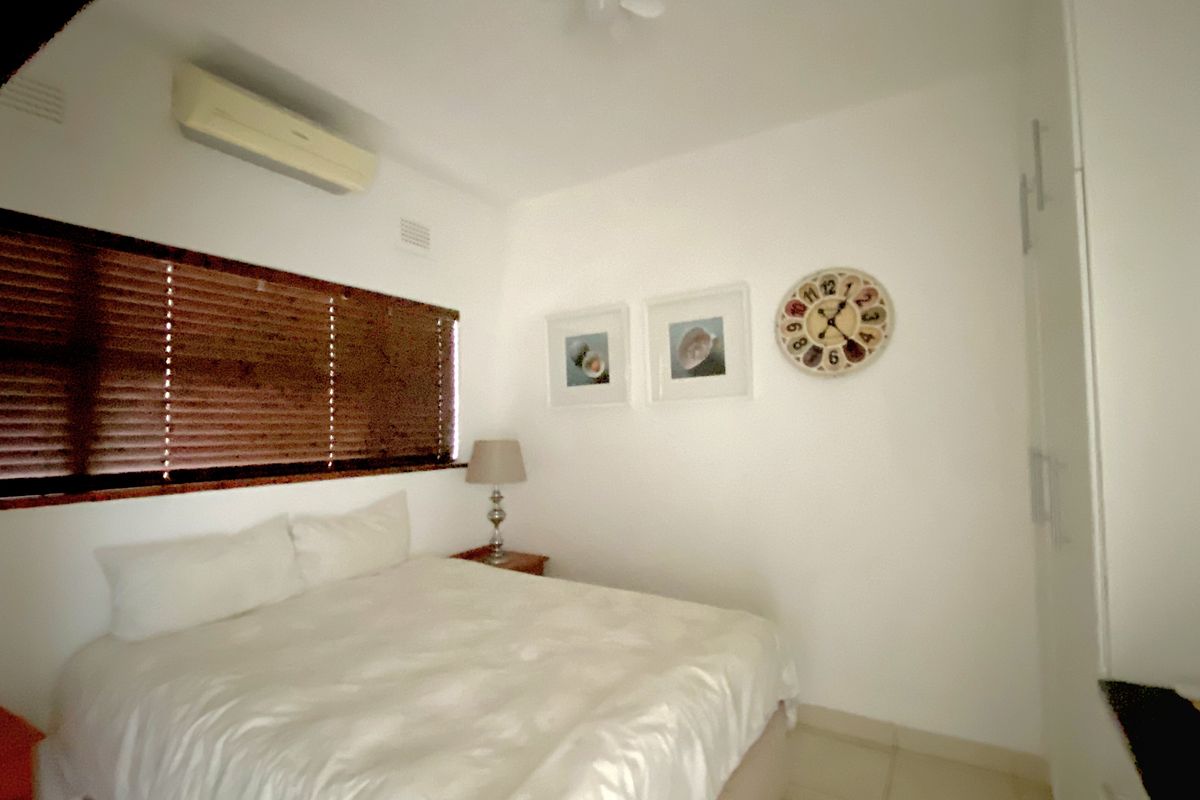 A bedroom featuring a wall-mounted air conditioning unit, built-in wardrobe, and wooden venetian blinds.