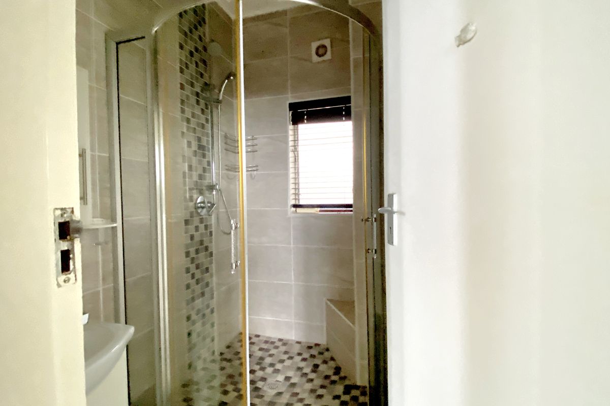 A compact bathroom featuring a corner shower enclosure with mosaic tile accents, tiled flooring, and a small window for natural light.