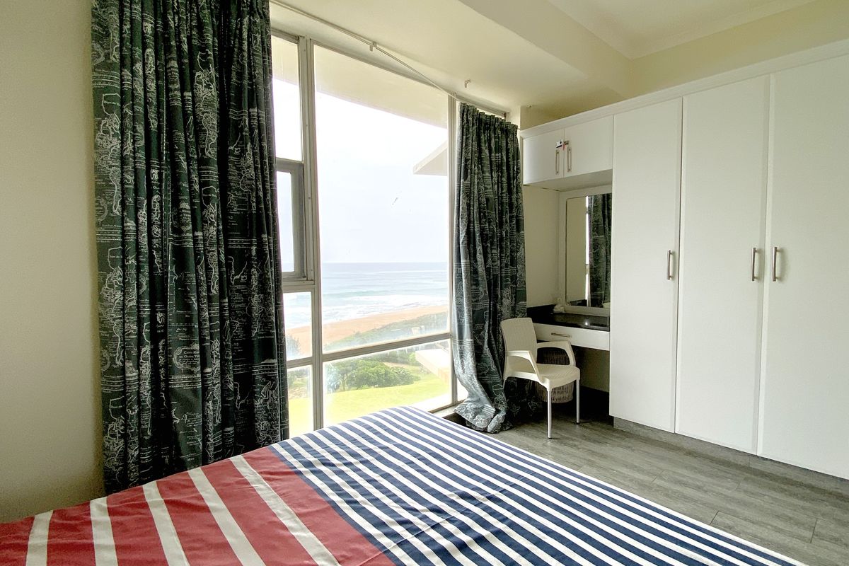 A bedroom featuring built-in white cabinetry with an integrated vanity and large windows offering a direct ocean view.
