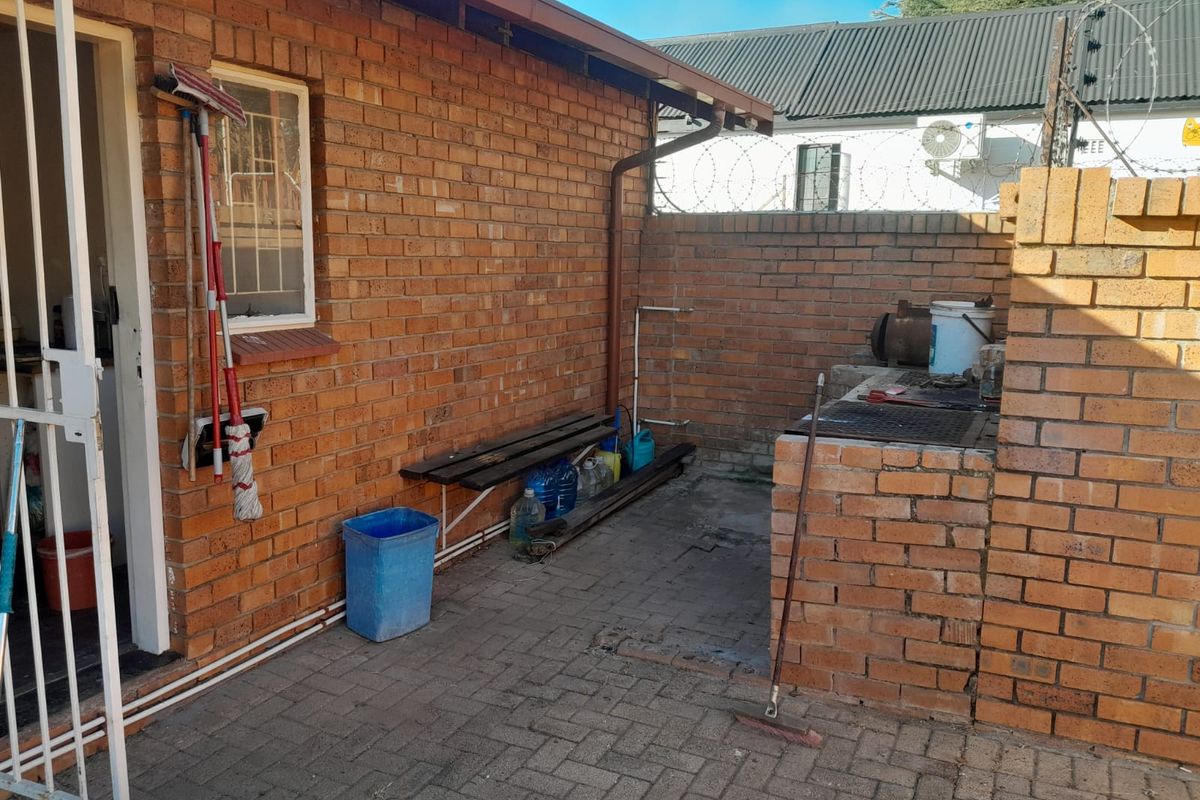 A rear courtyard area featuring a built-in brick braai, paved flooring, and direct access to the home via a security gate.