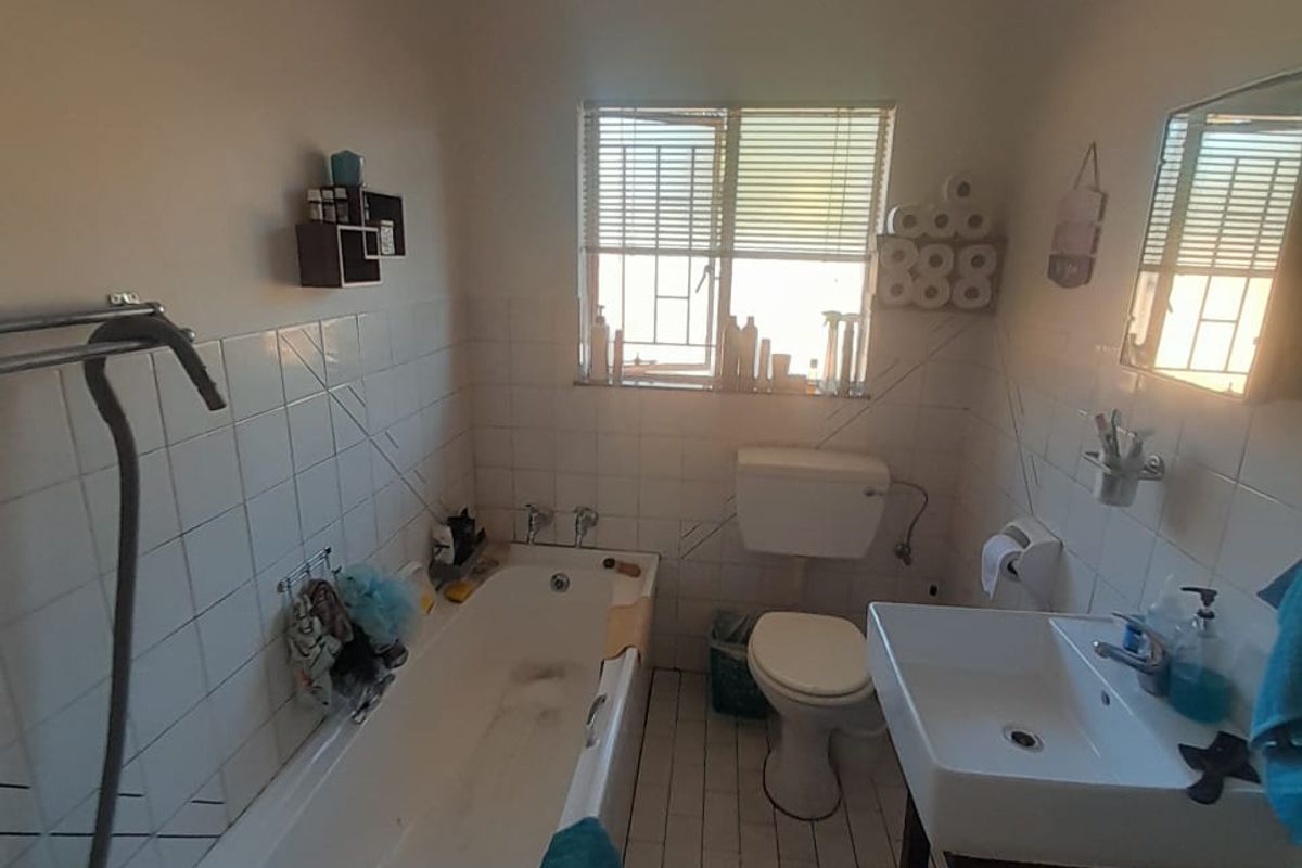 A functional bathroom featuring a bathtub, pedestal basin, and toilet, with white tiled walls and flooring, offering a practical layout for a townhouse.