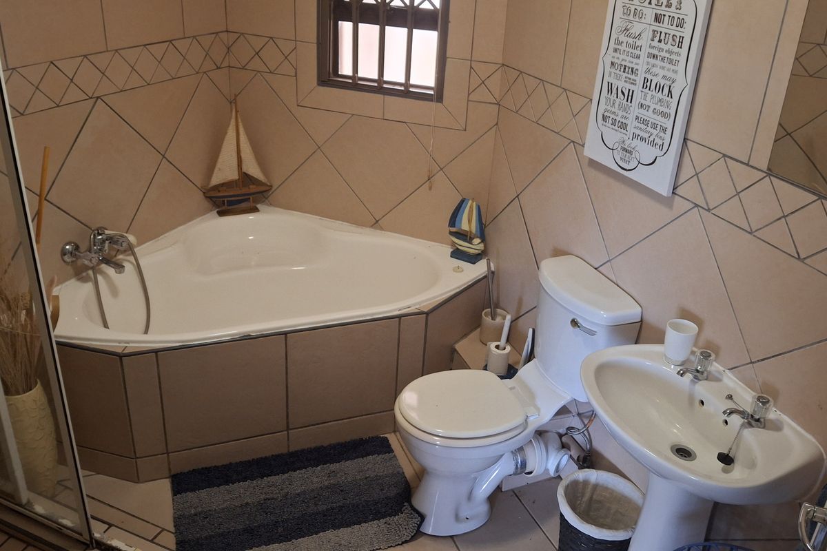 A compact bathroom featuring a corner bathtub, pedestal basin, and toilet with tiled walls and flooring.