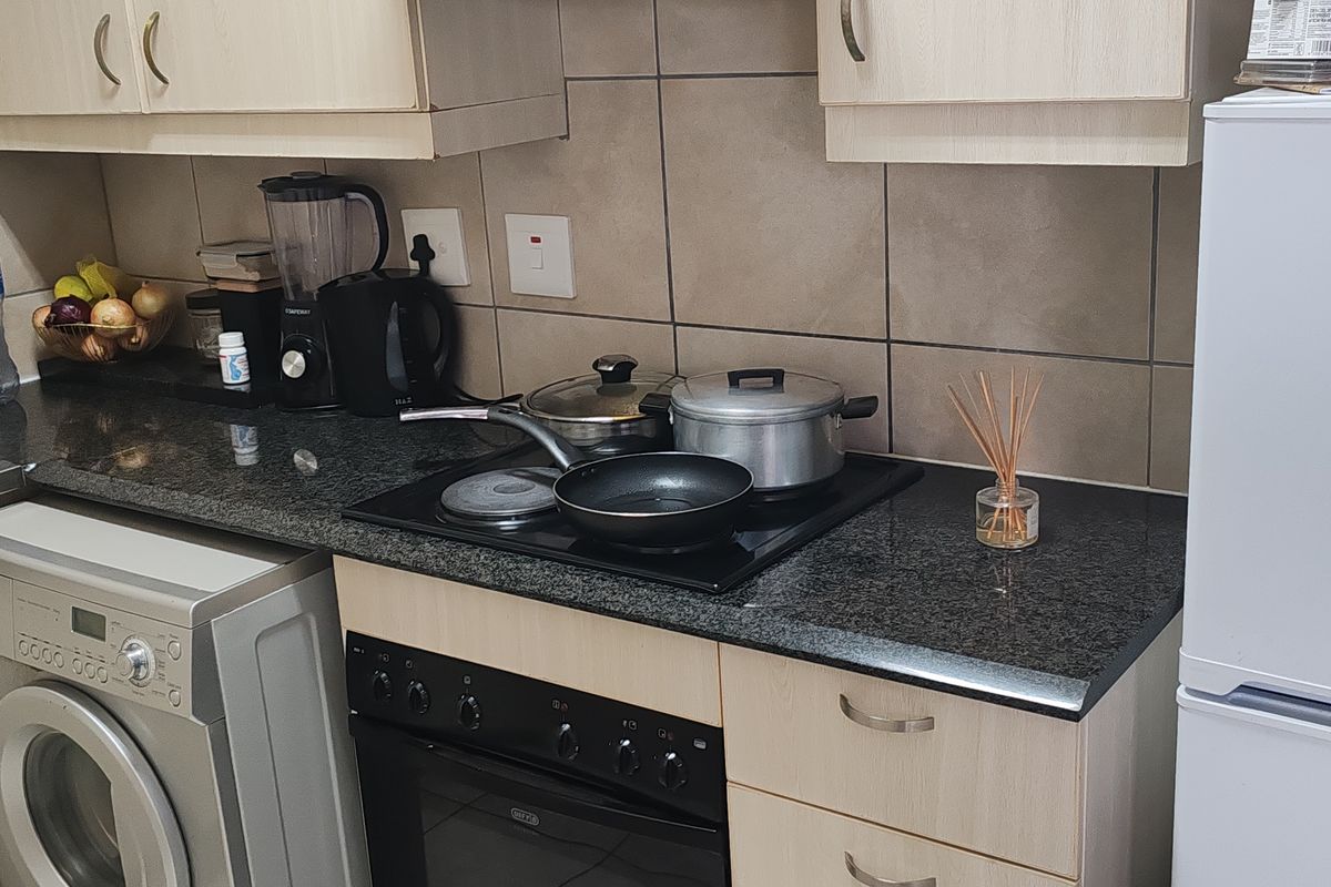 Compact kitchen featuring granite countertops, built-in oven with electric hob, light wood cabinetry, and integrated laundry appliance space.