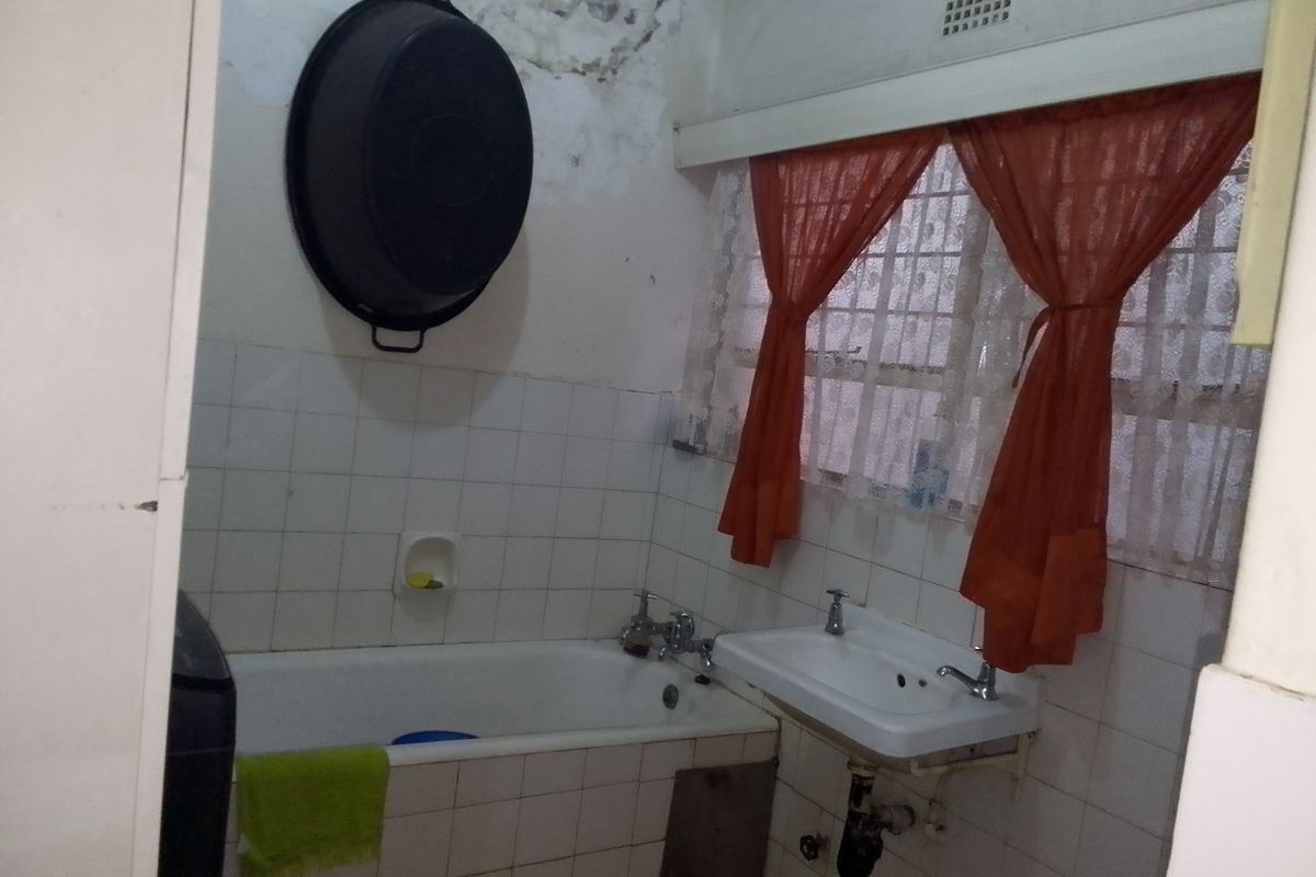 A dated bathroom featuring a standard bathtub and wall-mounted basin, requiring significant renovation and repair to address ceiling water damage and worn finishes.