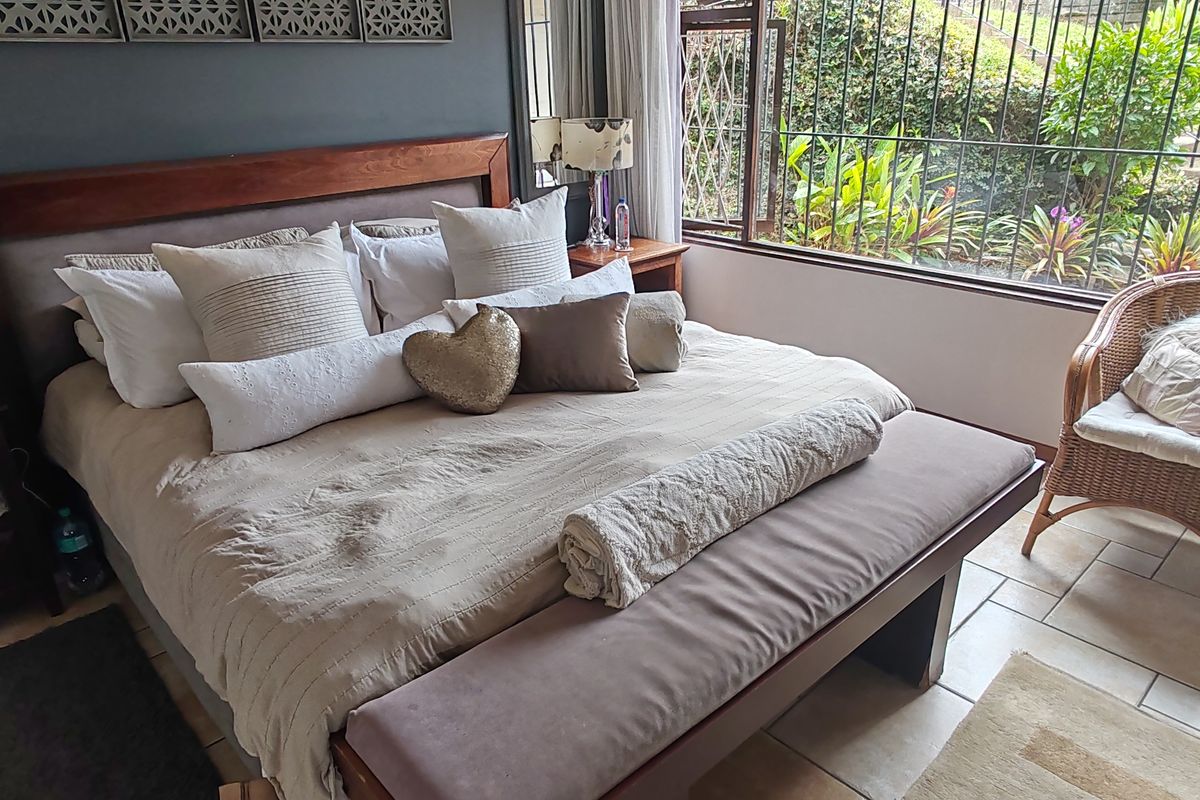 A bedroom featuring large windows with security bars, tiled flooring, and a neutral color palette, offering a view of the garden area.