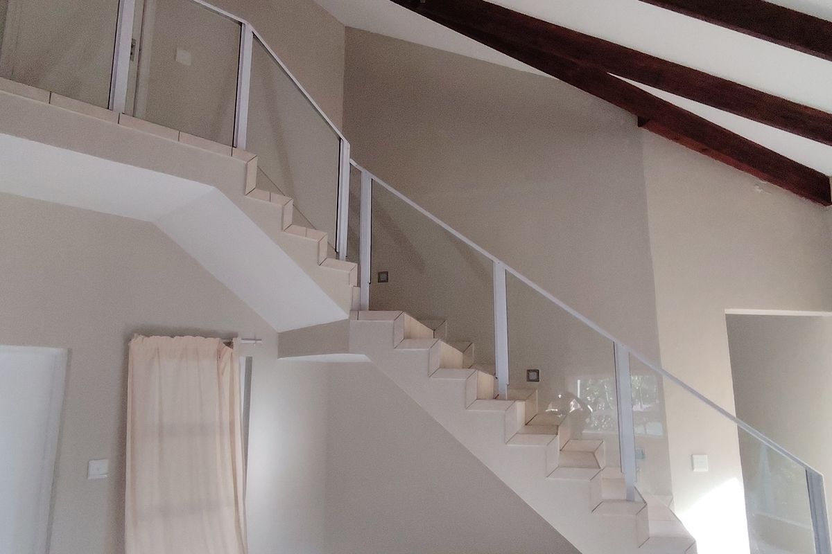 Spacious living area featuring a modern staircase with glass balustrades and striking exposed timber ceiling beams, creating an open and airy atmosphere.