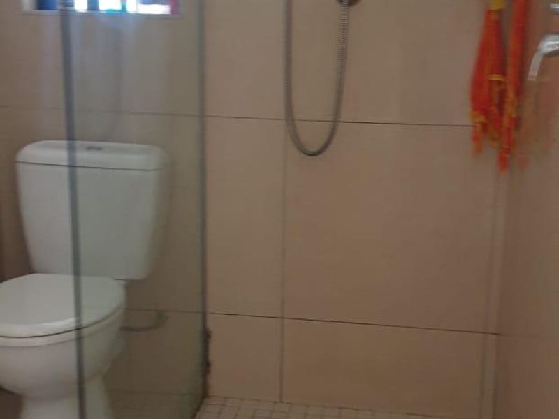 A functional bathroom featuring a glass-enclosed shower, wall-mounted shower fixtures, and tiled finishes throughout.