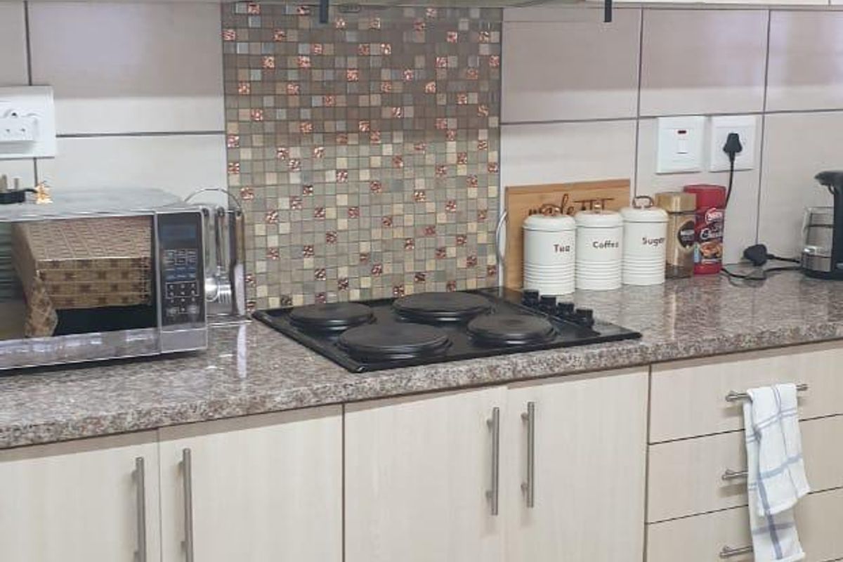 A functional kitchen featuring light wood-finish cabinetry, granite-look laminate countertops, a mosaic tile backsplash, and a built-in electric hob with an extractor fan.