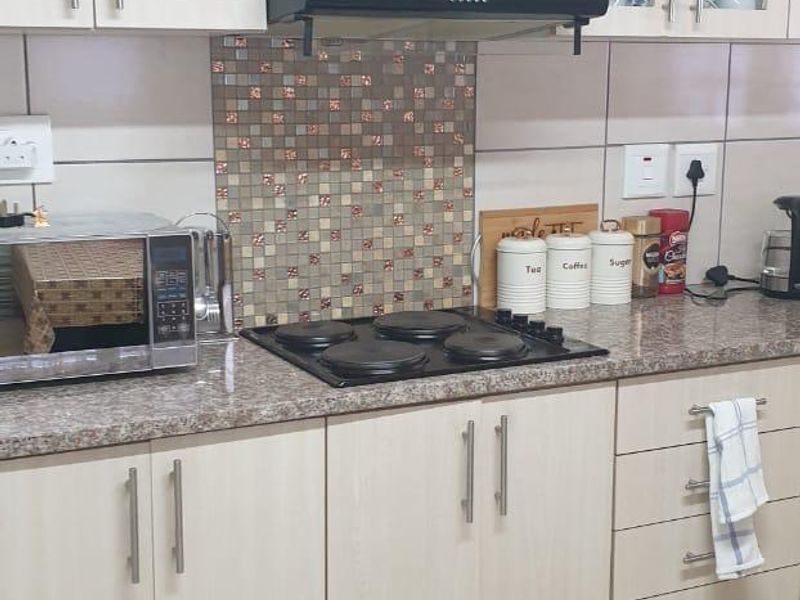 A functional kitchen featuring light wood-finish cabinetry, granite-look laminate countertops, a mosaic tile backsplash, and a built-in electric hob with an extractor fan.