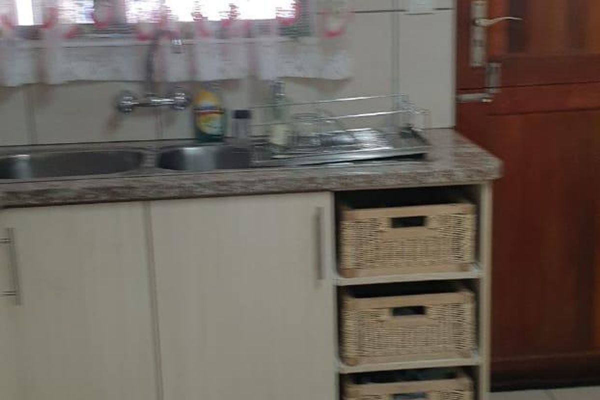 A functional kitchen area featuring built-in cabinetry, a double stainless steel sink, laminate countertops, and tiled finishes throughout.