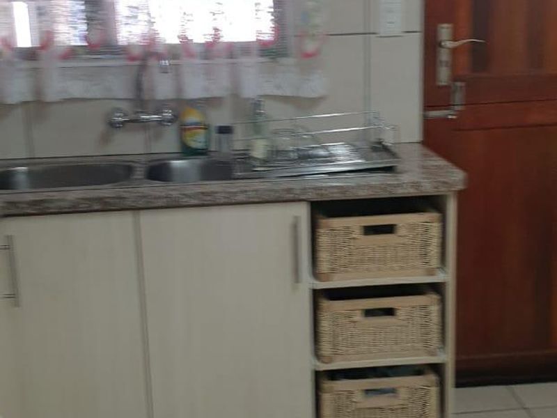 A functional kitchen area featuring built-in cabinetry, a double stainless steel sink, laminate countertops, and tiled finishes throughout.