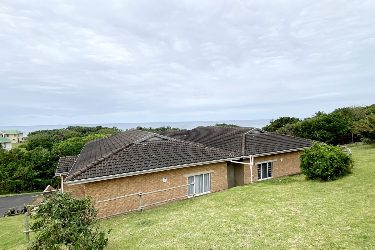 An elevated exterior view of a brick apartment building featuring a tiled roof, set within a landscaped garden with distant ocean views.