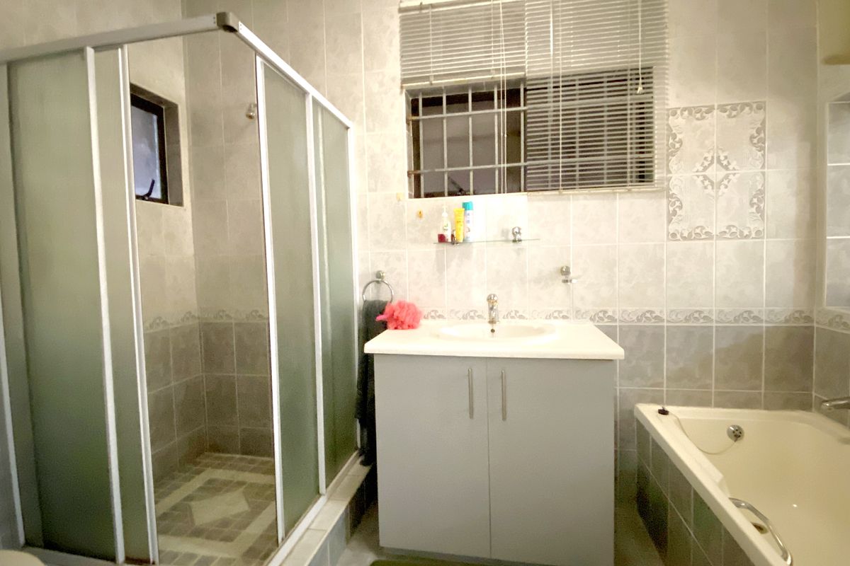 A functional bathroom featuring a separate shower enclosure, a built-in vanity with basin, and a bathtub, finished with neutral wall and floor tiling.