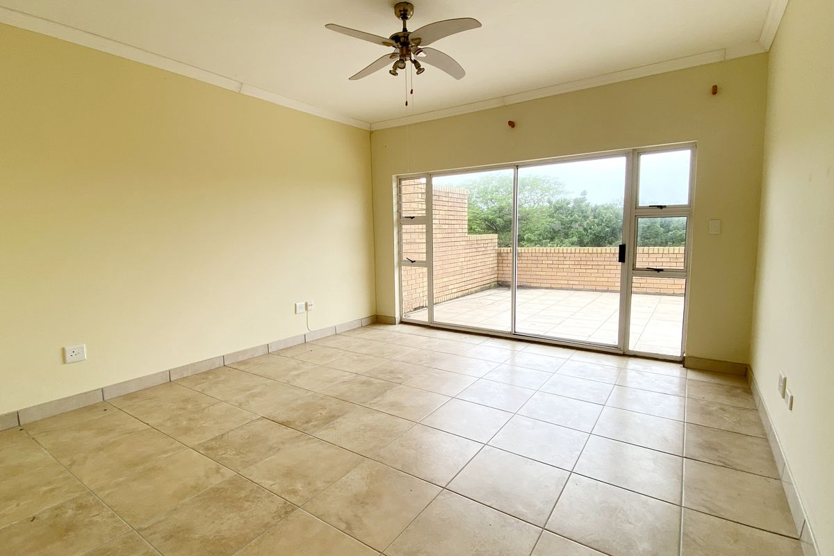 Spacious living area featuring neutral ceramic floor tiles, a ceiling fan, and large sliding glass doors providing direct access to an outdoor patio.