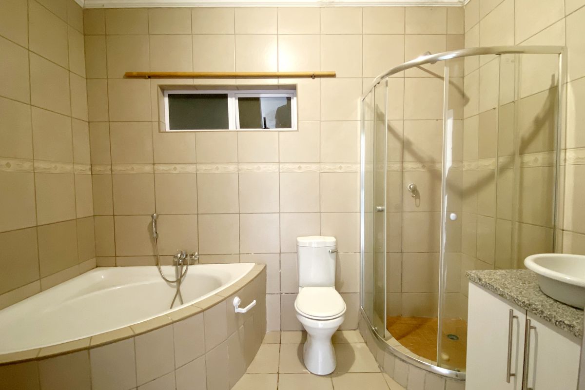 A functional bathroom featuring a corner bathtub, a separate curved glass shower enclosure, a toilet, and a vanity with a countertop basin.