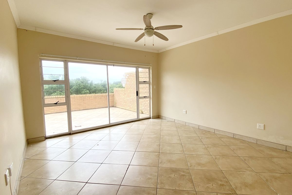 Spacious living area featuring tiled flooring, a ceiling fan, and large sliding glass doors providing direct access to an outdoor balcony.