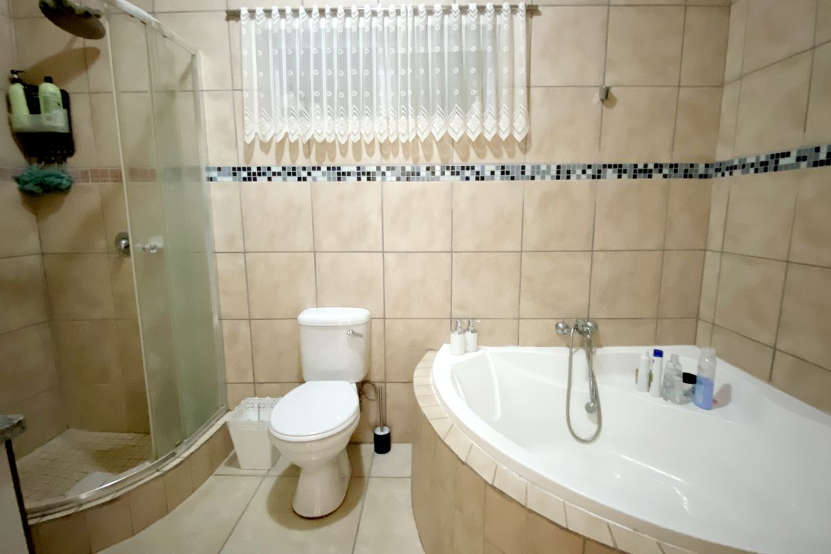 A functional bathroom featuring a corner bathtub, a separate glass-enclosed shower, and a standard toilet with neutral wall and floor tiling.
