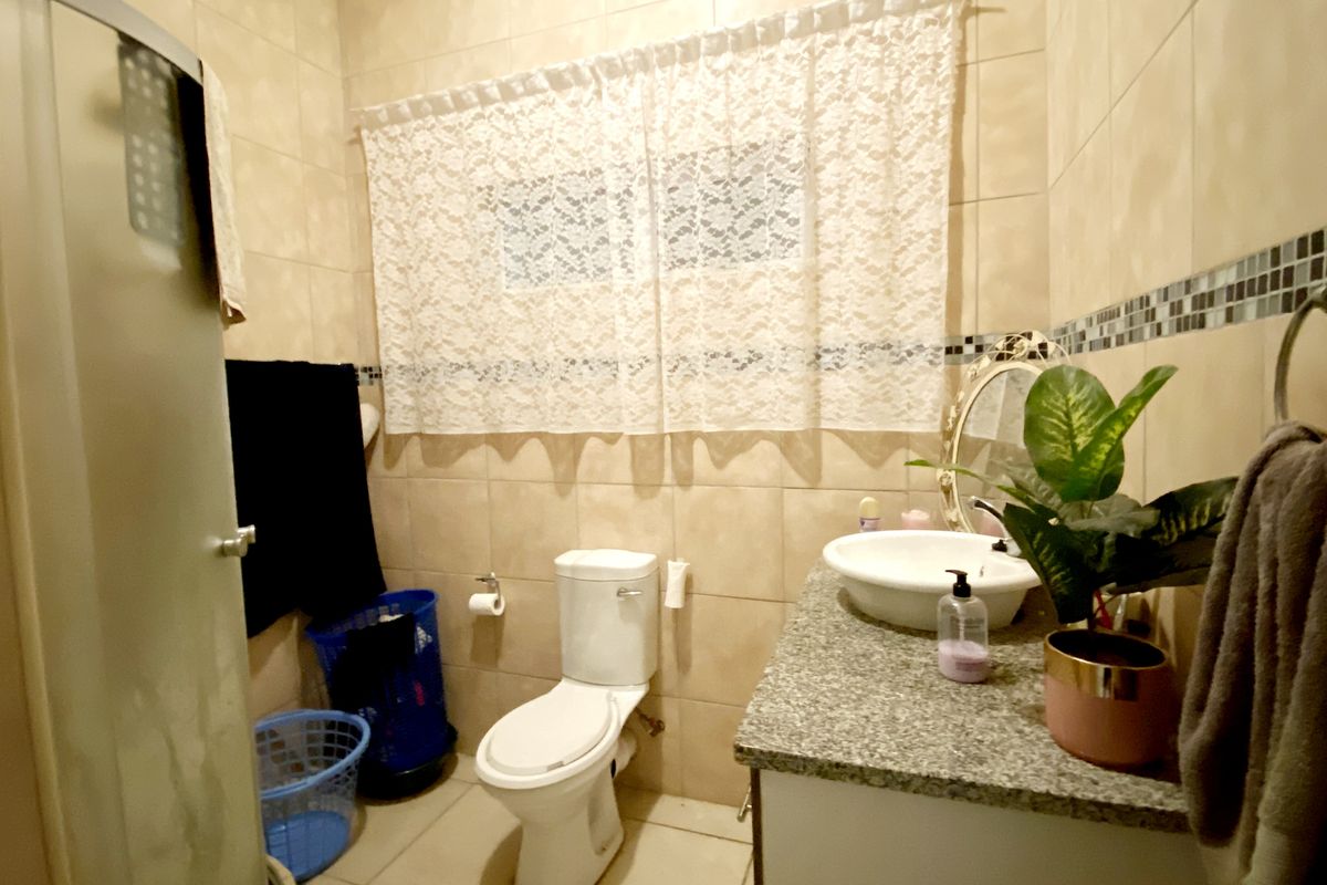 A functional bathroom featuring a vanity with a stone countertop, a ceramic basin, a toilet, and a shower enclosure with tiled walls.