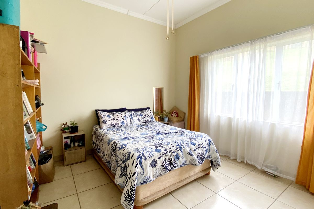 A bedroom featuring large windows with natural light, tiled flooring, and neutral wall tones, providing a functional and bright living space.