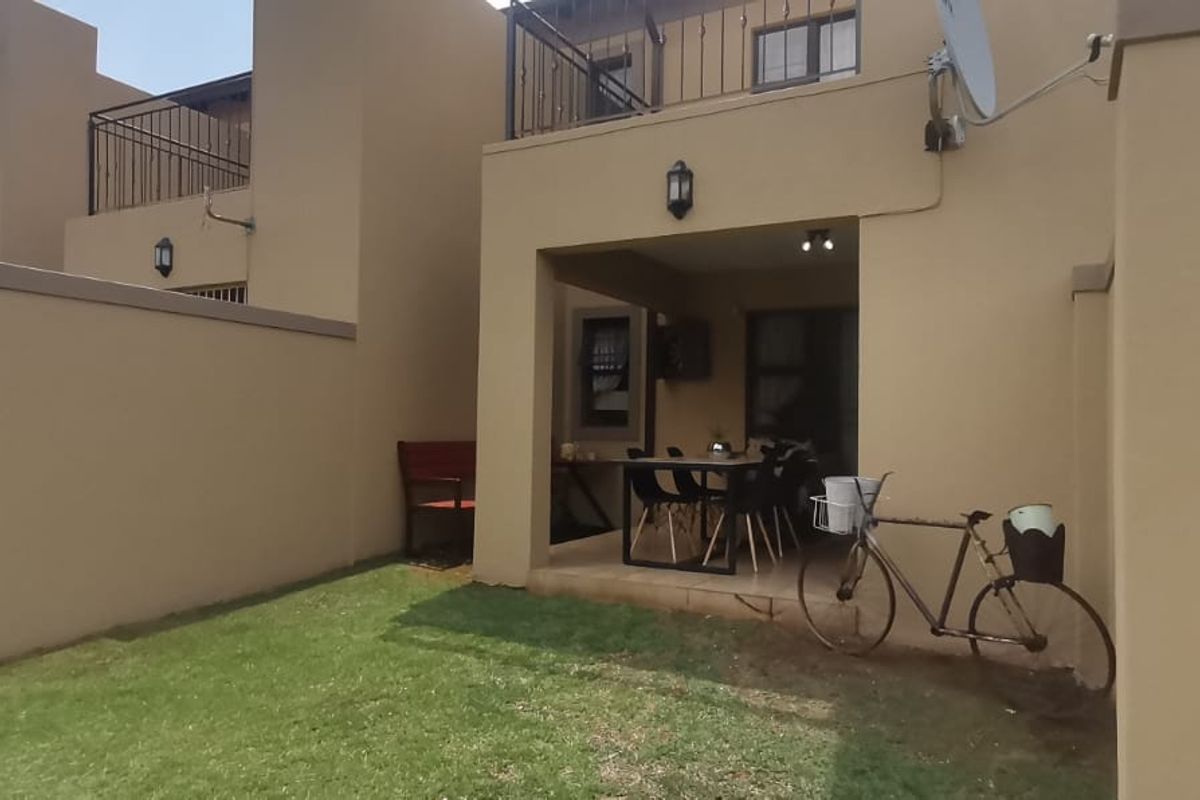Rear view of the apartment featuring a covered patio area, a small private garden, and an upper-level balcony with wrought iron railings.
