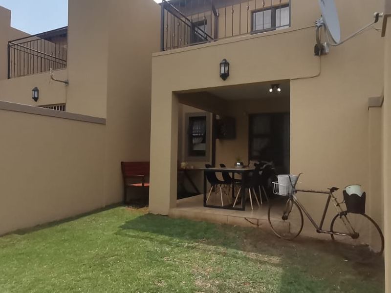 Rear view of the apartment featuring a covered patio area, a small private garden, and an upper-level balcony with wrought iron railings.