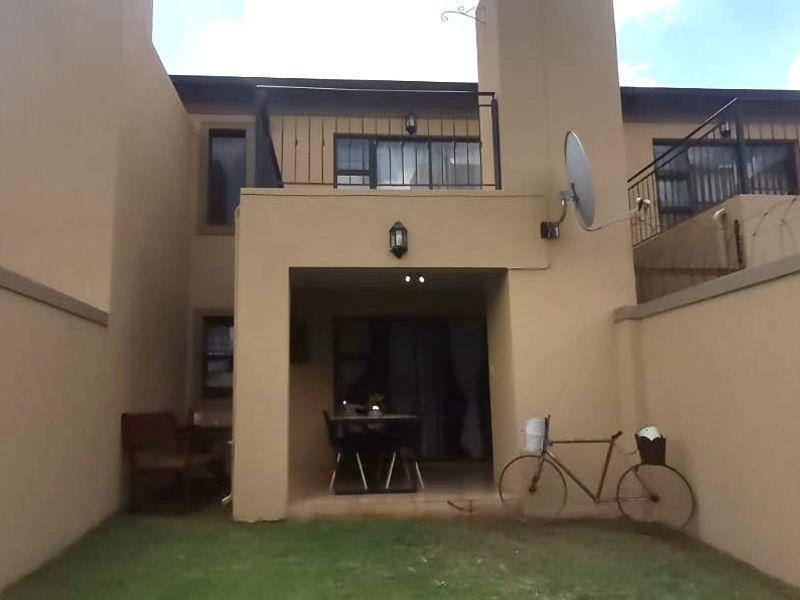 Rear view of the apartment complex featuring a ground floor covered patio, upper level balcony with metal railings, and small private garden area.