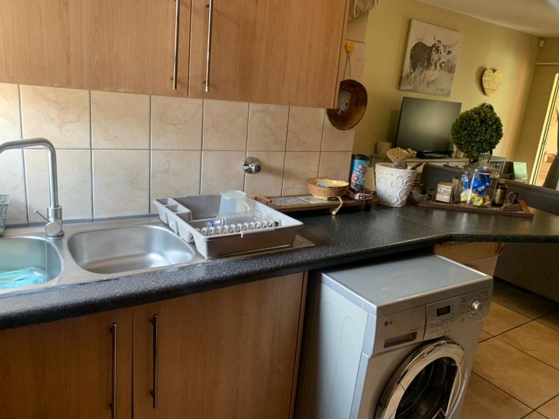 A functional kitchen area featuring laminate cabinetry, a stainless steel sink with mixer tap, tiled splashback, and an integrated washing machine.