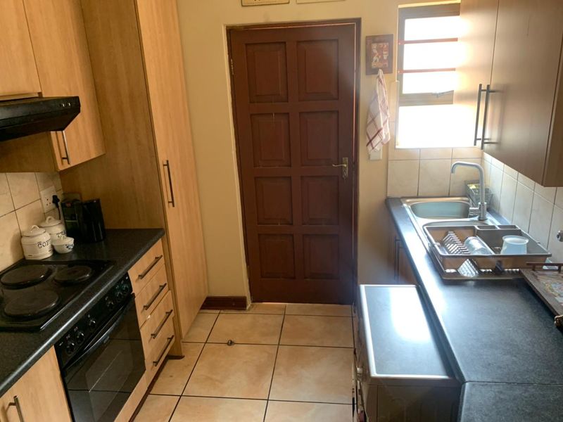 A functional kitchen featuring built-in cabinetry, laminate countertops, an electric hob, oven, extractor fan, and a stainless steel sink with tiled flooring.
