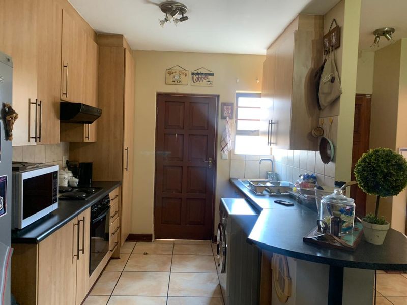 A functional kitchen featuring laminate cabinetry, dark countertops, built-in oven, extractor fan, and tiled flooring with a rear access door.
