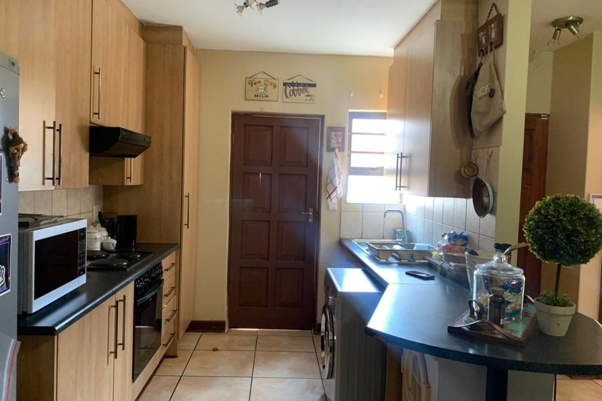 A functional kitchen featuring laminate cabinetry, dark countertops, built-in oven, extractor fan, and tiled flooring with a rear access door.