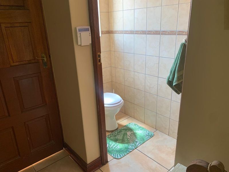 A compact guest bathroom featuring ceramic wall and floor tiling, a standard toilet, and a wooden door entrance.