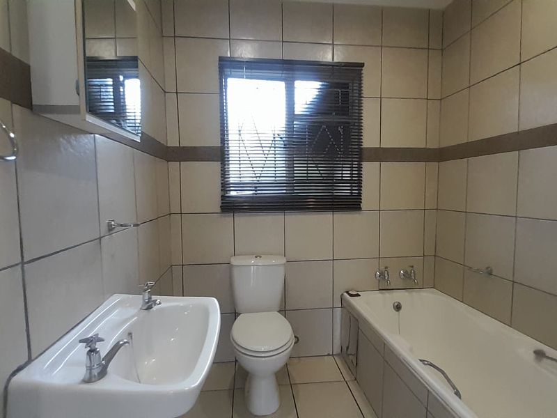 A functional bathroom featuring a bathtub, pedestal basin, and toilet with neutral wall and floor tiling.