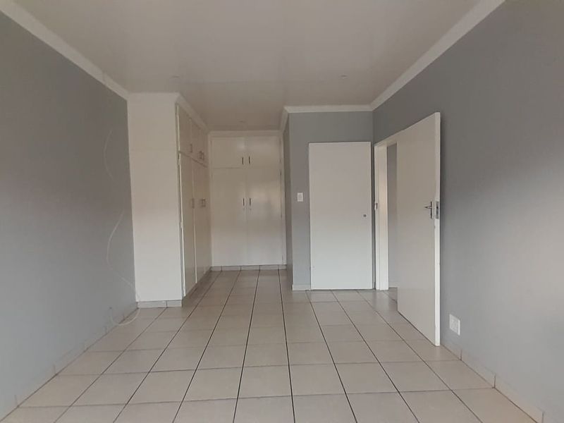 An empty bedroom featuring neutral grey walls, tiled flooring, and ample built-in cupboard storage space.