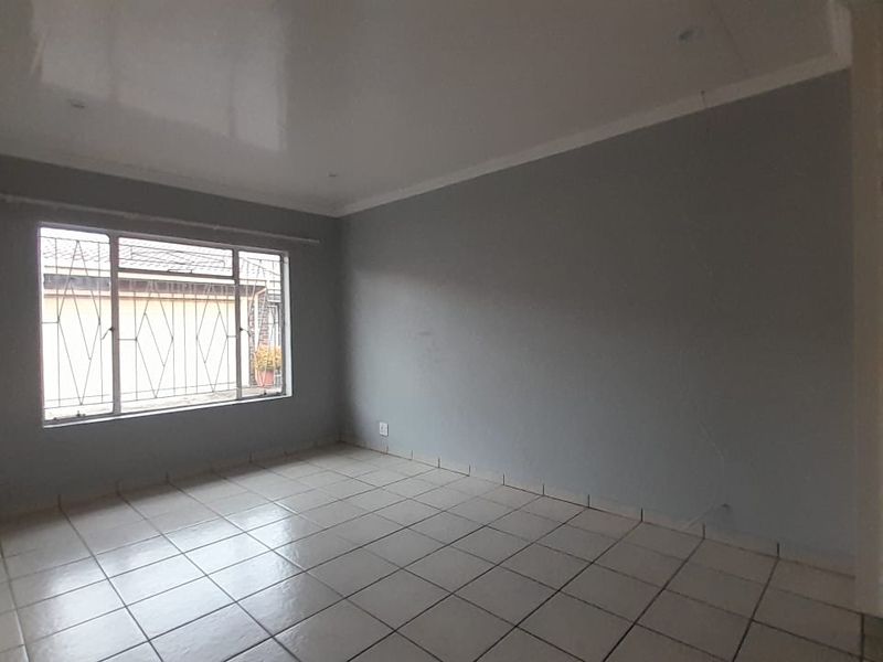 An empty living room featuring tiled flooring, neutral grey walls, and a window fitted with security bars.