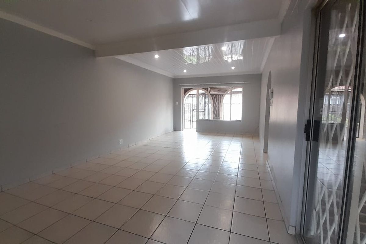 A spacious, empty living area featuring neutral tiled flooring, recessed lighting, and a sliding glass door with security gate leading to the exterior.