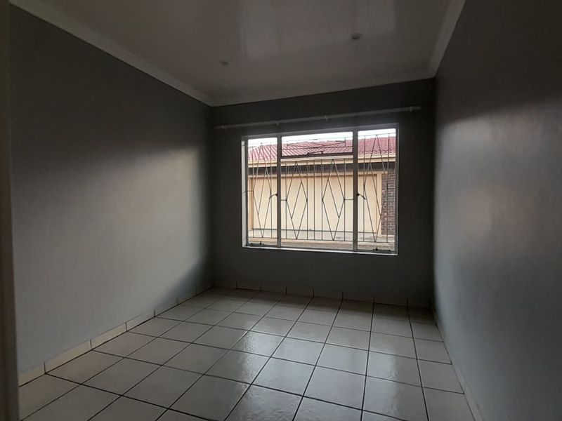 An empty bedroom featuring neutral grey walls, tiled flooring, and a window fitted with security bars.