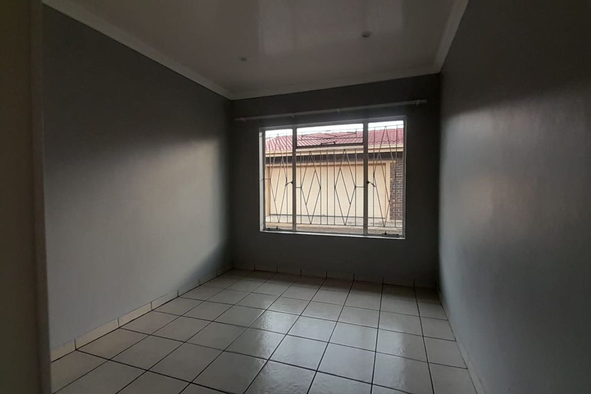 An empty bedroom featuring neutral grey walls, tiled flooring, and a window fitted with security bars.