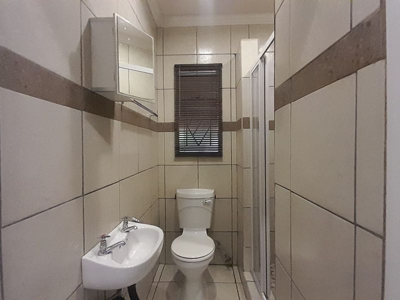 A functional bathroom featuring a shower enclosure, wall-mounted basin, and toilet, finished with neutral wall and floor tiles.