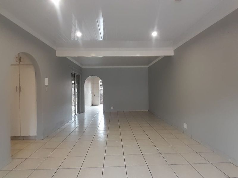 A spacious, empty living area featuring neutral grey walls, tiled flooring, recessed lighting, and distinctive arched architectural details.