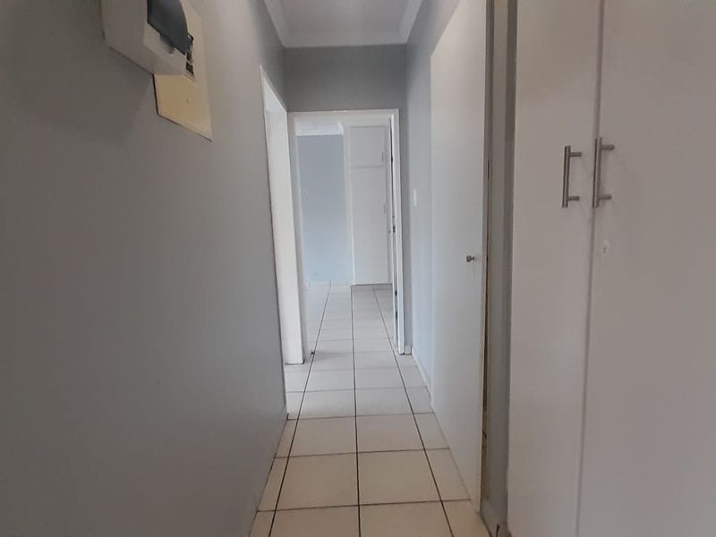 A clean, neutral hallway featuring tiled flooring and built-in storage cupboards, providing access to other areas of the townhouse.