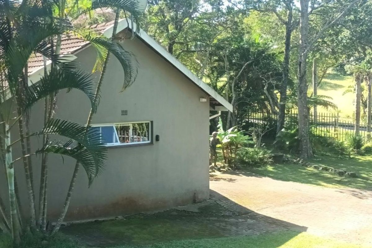 Side view of the house exterior featuring a tiled roof, plastered walls, and a paved driveway area surrounded by established trees and garden.