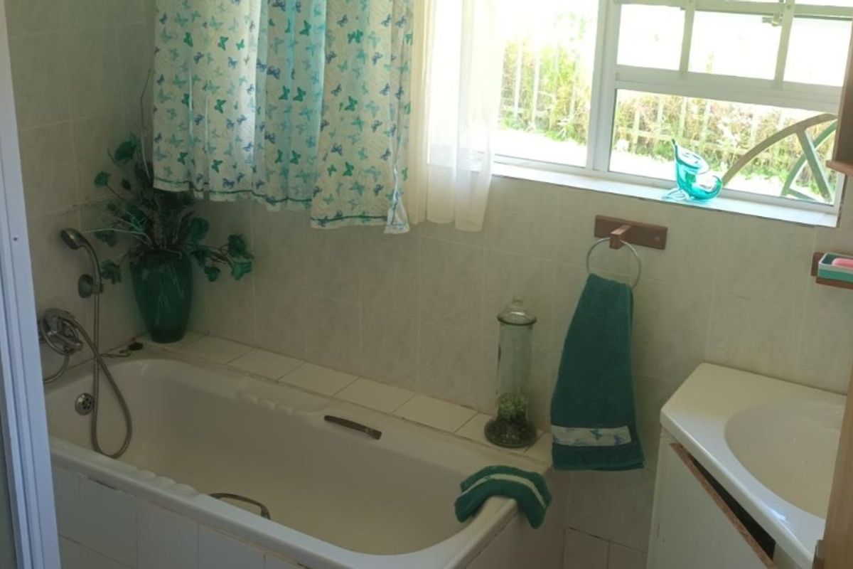 A functional bathroom featuring a built-in bathtub with shower attachment, a vanity basin, and a window providing natural light.