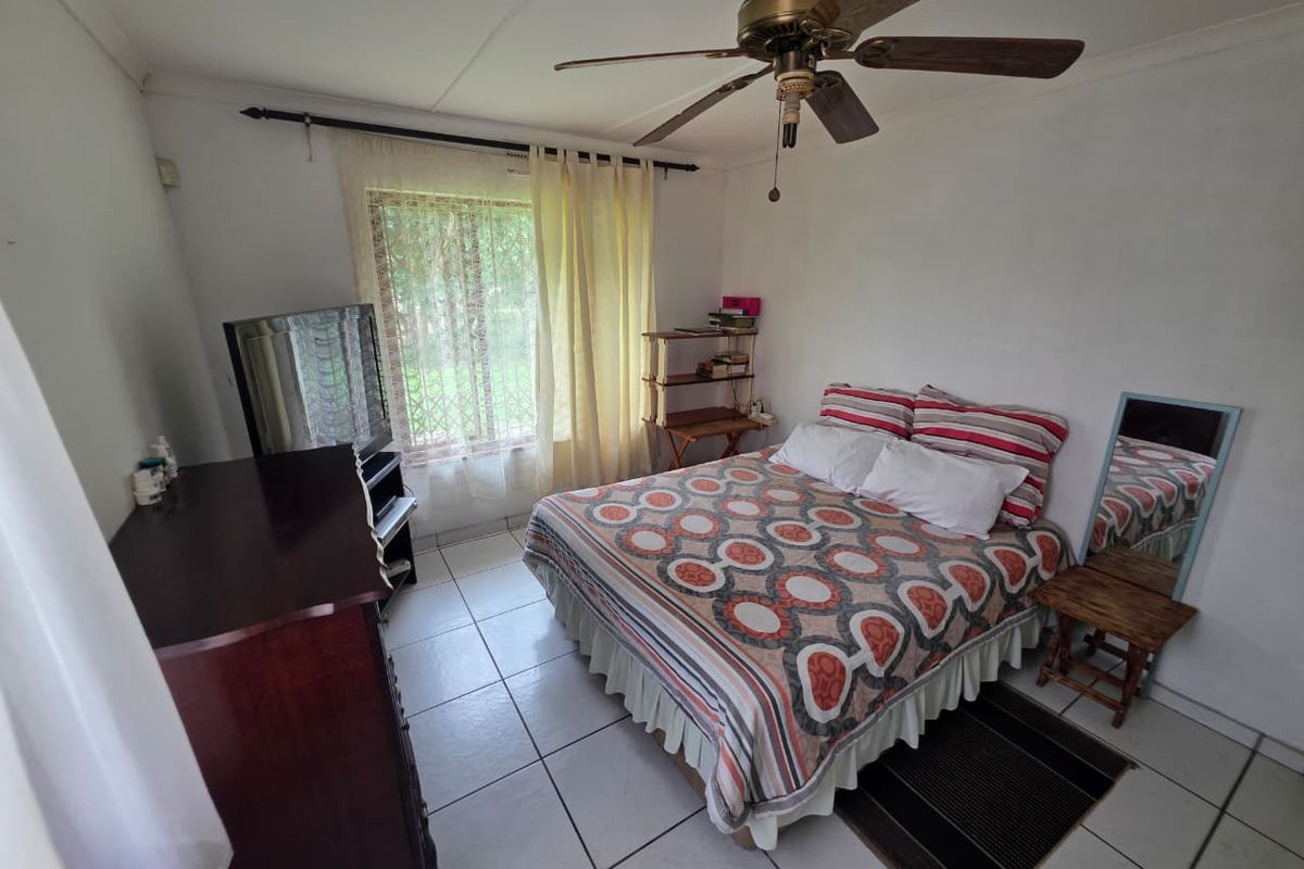 A functional bedroom featuring tiled flooring, a ceiling fan, and a window with security bars, offering a basic layout ready for cosmetic updates.