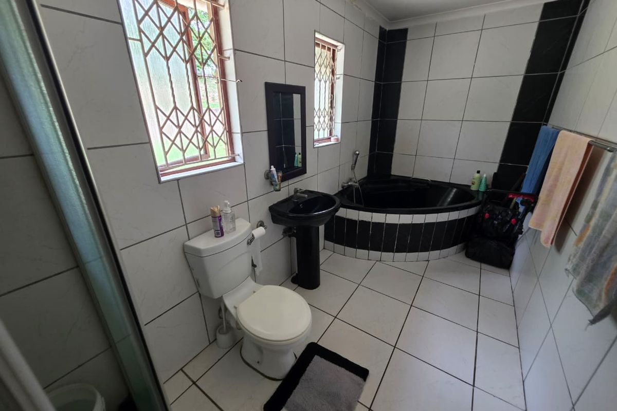 A dated bathroom featuring a corner bathtub, pedestal basin, and toilet with black and white tiled finishes and security bars on the windows.