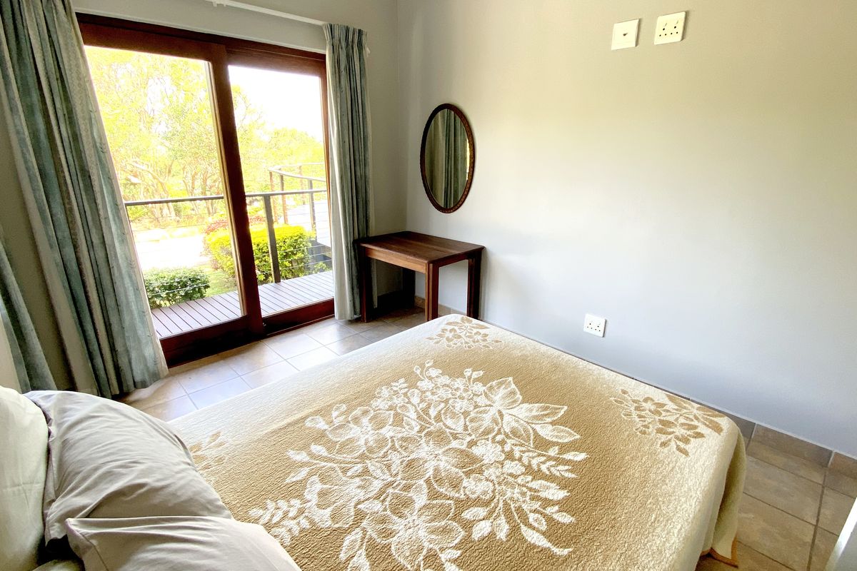 A bedroom featuring tiled flooring and sliding glass doors that open onto a private balcony with garden views.