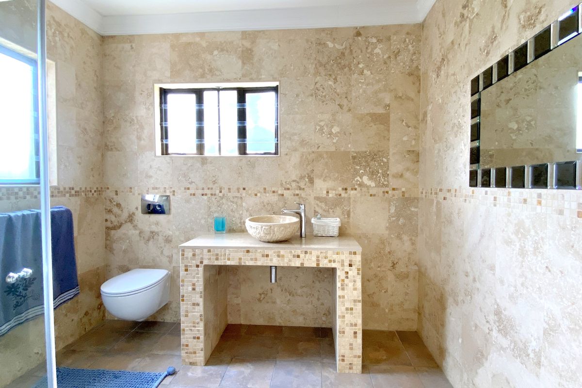 A well-appointed bathroom featuring natural stone wall tiling, a floating toilet, and a custom-built vanity with a stone vessel sink.