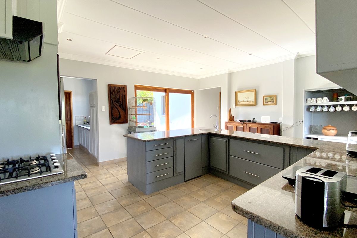 Spacious kitchen featuring a large central island, granite countertops, built-in gas hob, and an adjoining scullery area with tiled flooring throughout.