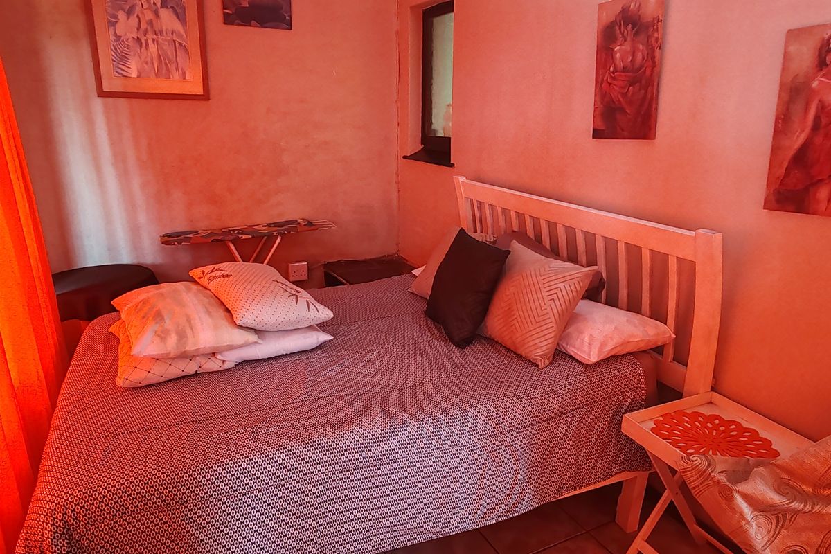 A bedroom featuring tiled flooring and a built-in headboard, characterized by a warm, reddish ambient lighting.
